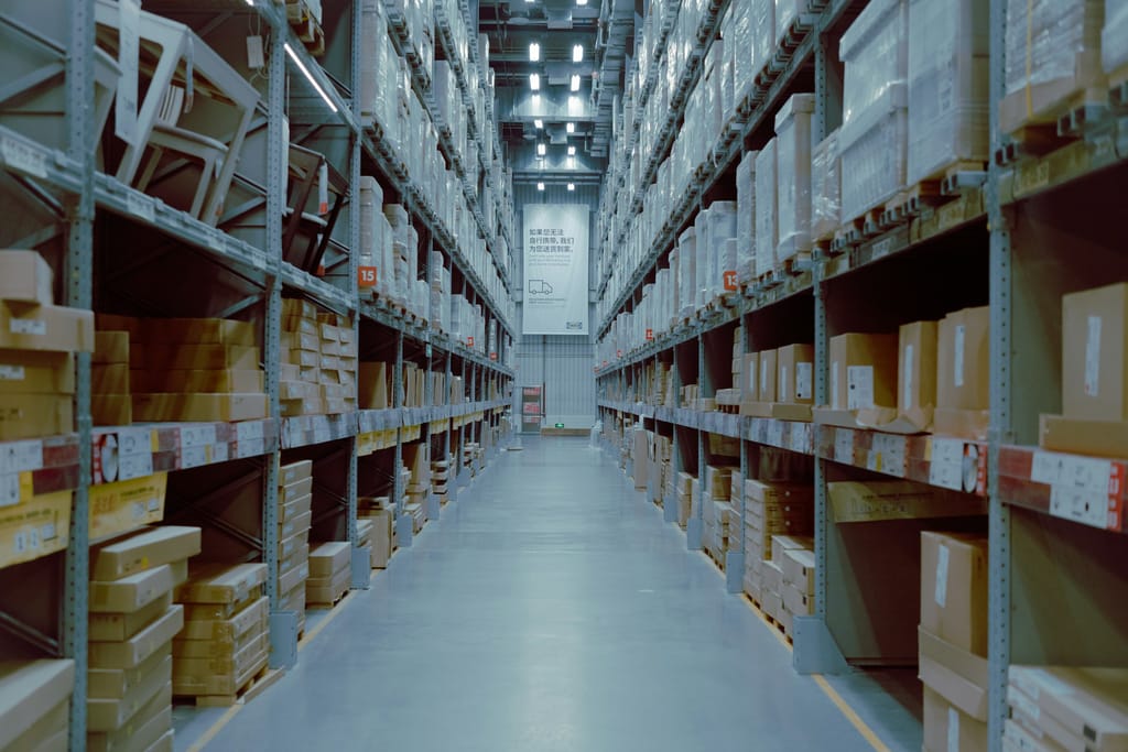 Stacked cardboard boxes and packaged goods on shelving, illustrating general wholesale supply categories.